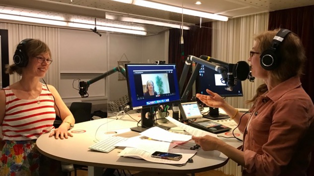 Delmi-poddens programledare i studion med en gäst framför sig och en gäst som deltar via Skype.