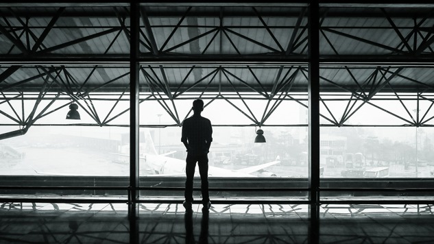 A man at the airport standing with his back against the camera and looking out over the airport field.