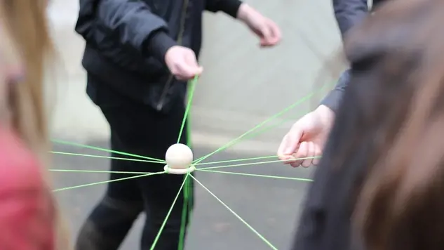 Flera personer som leker en lek med en boll och gröna trådar. Bild: Unsplash.
