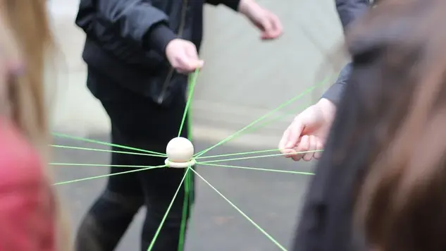 Several people playing a game with a ball and green threads. Picture: Unsplash.
