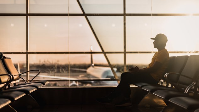 En ung man som sitter på en flygplats och kollar ut på flygfältet. Bild: Unsplash.