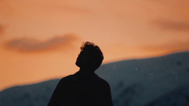 A man looking up towards the pink sky with mountains in the background. Picture: Unsplash.
