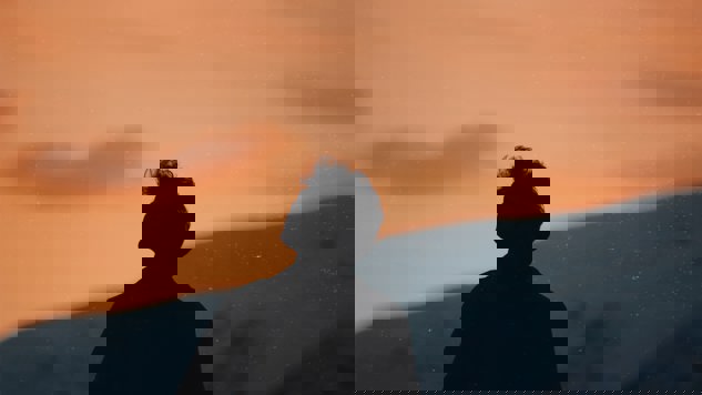 En man som tittar upp mot den rosa himlen med berg i bakgrunden. Bild: Unsplash.