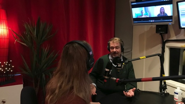 Delmi-poddens programledare sitter vid ett bord med en gäst och två gäster syns på en skärm.