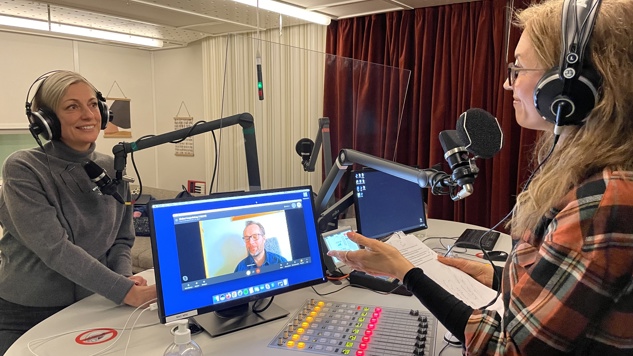 Delmi-poddens programledare i studion med en gäst framför sig och en gäst som deltar via Skype.
