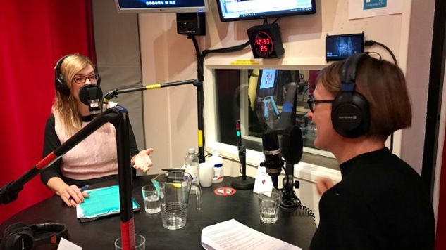 Två personer som sitter vid ett runt bord med manus framför sig.