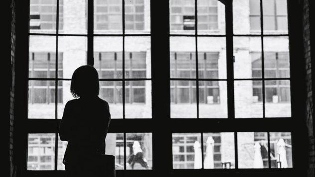 A black and white image of a woman standing by a window. Picture: Unsplash.
