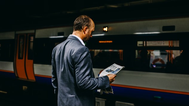 En man som står vid tågperrongen och läser en tidning. Bild: Unsplash.