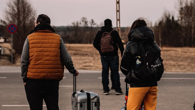 Tre personer står vid en vägkant med resväskor. Bild: Unsplash.